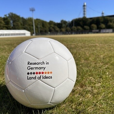 A football lies on a lawn. "Research in Germany - Land of Ideas" is written on the ball.