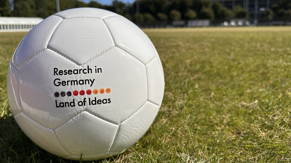 A football lies on a lawn. "Research in Germany - Land of Ideas" is written on the ball
